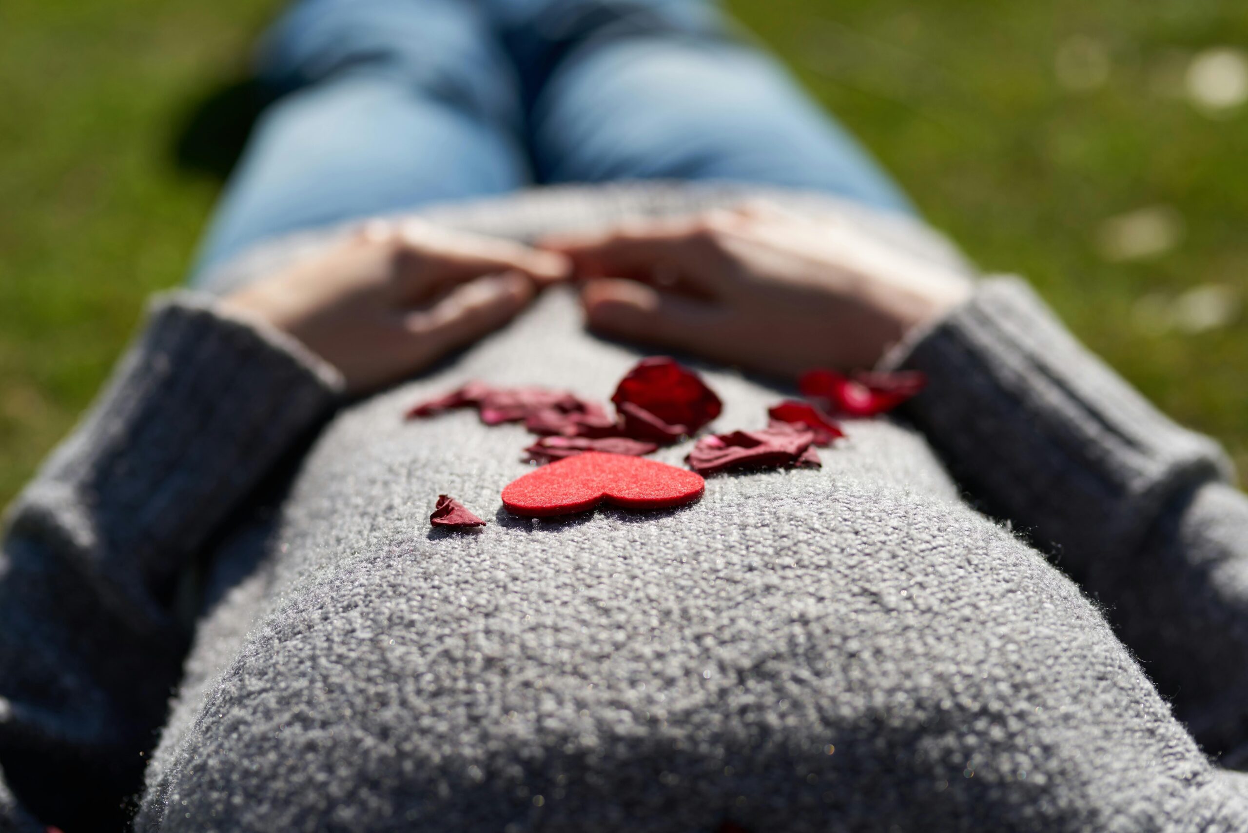 femme allongée dans l'herbe avec petales de fleur rouge sur le ventre